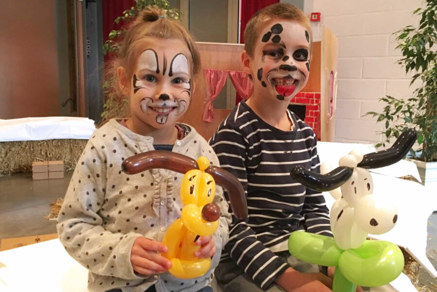 Des enfants avec des maquillage tenant chacun une sculpture de ballons d'une chien et d'une vache.