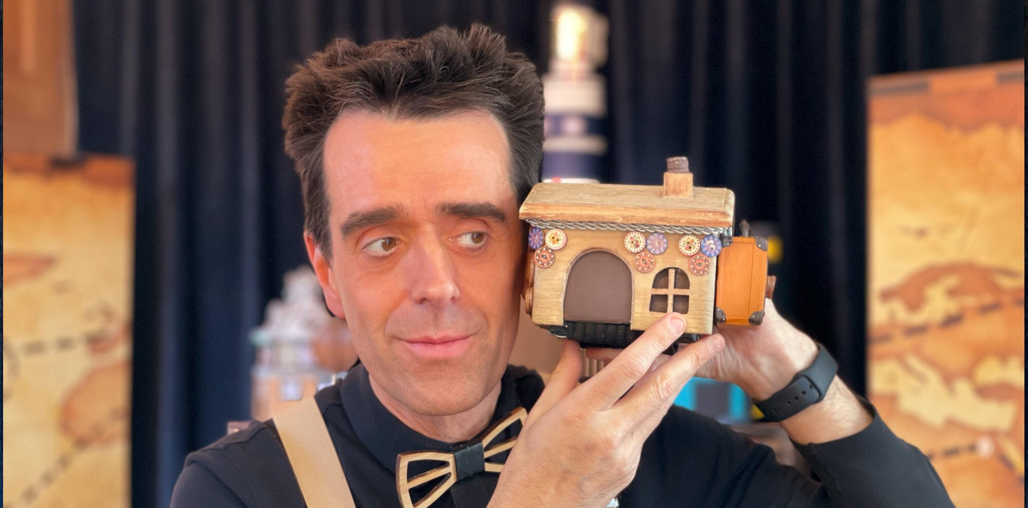Risque-Tout Monsieur Fred sur scène avec le décor de l’île et du village, présentant le spectacle “Risque-Tout” pour jeunes enfants.